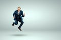 A man in a business suit jumps up cheerfully against a light background. The concept of joy, success, luck, winning