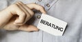 A man businessman in a blue shirt holds a card in a pocket with the text Beratung in his hand