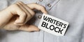 A man businessman in a blue shirt holds a card in a pocket with the text Writer`S Block in his hand Royalty Free Stock Photo