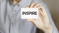 A man businessman in a blue shirt holds a card with the text Inspire in his hand