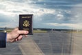 Man businessman in a blue suit holding american passport in the airport waiting zone looking through the window at planes.