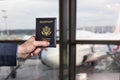 Man businessman in a blue suit holding american passport with in the airport waiting zone looking through the window at planes