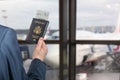 Man businessman in a blue suit holding american passport with boarding pass in the airport waiting zone looking through the