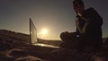 Man businessman freelancer talking on the phone working behind laptop sitting on beach freelancing silhouette in the sun Royalty Free Stock Photo