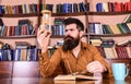 Man on busy face reading book, bookshelves on background. Lesson and time concept. Scientist with eyeglasses sits at Royalty Free Stock Photo