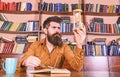 Man on busy face reading book, bookshelves on background. Lesson and time concept. Scientist with eyeglasses sits at Royalty Free Stock Photo