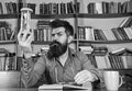 Man on busy face reading book, bookshelves on background. Lesson and time concept. Teacher or student with beard Royalty Free Stock Photo