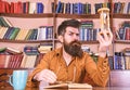 Man on busy face reading book, bookshelves on background. Lesson and time concept. Teacher or student with beard Royalty Free Stock Photo