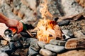 Man with a butane can burner kindles a fire in a bonfire on a stone beach