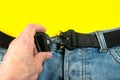 A man buttoned a black cloth belt on jeans. Modern men`s waistband with dark matted metal buckle