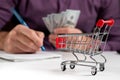 Man calculates the budget. Shopping cart a on table with calculator and paper and mohey in hadns Royalty Free Stock Photo