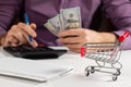 Man calculates the budget. Shopping cart a on table with calculator and paper and mohey in hadns Royalty Free Stock Photo