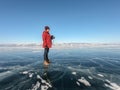 man with camera and bright orange winter jacket and knitted hat stands on icy frozen lake Baikal