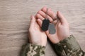 Man in camouflage uniform holding military ID tags over wooden background