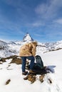 A man in camouflage winter coat sets up his backpack, standing in front of the background of Matterhorn, Royalty Free Stock Photo