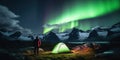 A man camping in wild northern mountains with an illuminated tent viewing a spectacular green northern lights aurora display