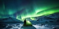 A man camping in wild northern mountains with an illuminated tent viewing a spectacular green northern lights aurora display