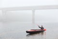 Man canoeing in traditional wooden kayak on large lake at cold cloudy day, fog over water, handsome guy wearing black jacket and Royalty Free Stock Photo