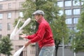 A man in a cap juggles with clubs on the street