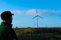 A man in a cap looks at the spinning wind turbines against the blue sky.