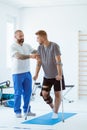 Man after car accident in an orthosis and on crutches learning to walk in the clinic, helpful therapist near him Royalty Free Stock Photo