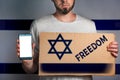 A man with a cardboard and a phone in his hand. The Flag Of Israel. Concept of freedoms and human rights. Text freedom, mock up