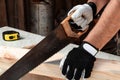 A man carpenter cuts a wooden beam using a handsaw, male hands with a saw closeup. Work with wood