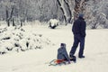 A man carries a child in a sled. Winter in the park