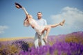 A man carries his woman in his arms through a lavender field, love, romantic relationships, the girl rejoices. Beautiful blonde in