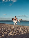 Man carries woman in white dress, couple happy on vacation. Couple in love stand on beach, seashore. Couple in love