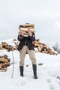 Man is carrying an armload of chopped wood in a rustic courtyard, on a frosty winter day. Heating season in the village. Royalty Free Stock Photo