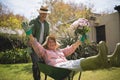 Man carrying cheerful senior woman holding bouquet in wheel borrow