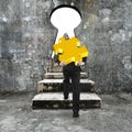 Man carrying golden jigsaw puzzle climbing concrete stairs toward keyhole Royalty Free Stock Photo