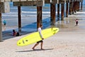 A man carrying a yellow surfboard walks along the beach near the surf