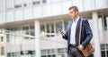 Man in casual business attire checks his phone walking outdoors in an office buildings environment Royalty Free Stock Photo
