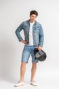 A man in a casual denim jacket and shorts holds a protective motorcycle helmet Royalty Free Stock Photo
