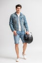 A man in a casual denim jacket and shorts holds a protective motorcycle helmet Royalty Free Stock Photo