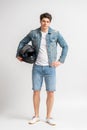 A man in a casual denim jacket and shorts holds a protective motorcycle helmet Royalty Free Stock Photo