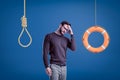 Man in casual outfit standing half-turn with hand on forehead as if choosing between lifebuoy hanging on rope and Royalty Free Stock Photo