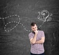 A man in casual shirt is thinking about unanswered questions. Question marks are drawn on the black chalkboard. Royalty Free Stock Photo