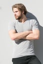 Man in casual tshirt with folded muscular hands. Guy with bearded unshaven face on grey wall. Macho with blond hair on sunny outdo