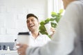 A man in casual white shirt is laughing and drinking coffee while having a meeting with his colleagues in the greenery white Royalty Free Stock Photo