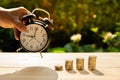 Man catch alarm clock and the money coins bar stack on wood table and sunset background in the public park show savings the money Royalty Free Stock Photo