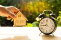 Man catch home model and the alarm clock stack on wood table and sunset background in the public park show Time to invest Royalty Free Stock Photo