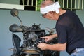 A man of Caucasian descent is fixing his malfunctioning motorbike.