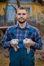 A man caucasian farmer satisfied portrait smiling in a shirt and overalls, holds a two dwarf white chickens close up in his hands Royalty Free Stock Photo