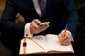 Man with cellphone sitting at a table working on his notebook Royalty Free Stock Photo