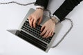 Man with chained hands typing on laptop against white background, top view. Internet addiction Royalty Free Stock Photo