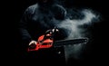 A man with a chainsaw in his hands close up against the background of smoke