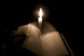 A man changes bible pages in front of a candle